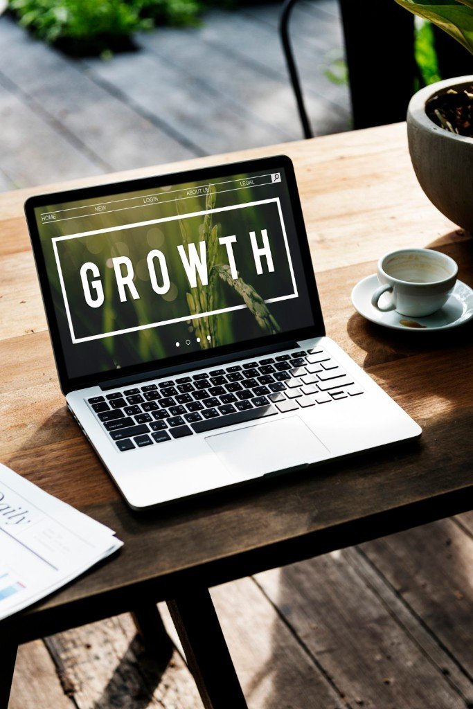 A laptop on a wooden table displaying a professional website with the word GROWTH in bold letters.
