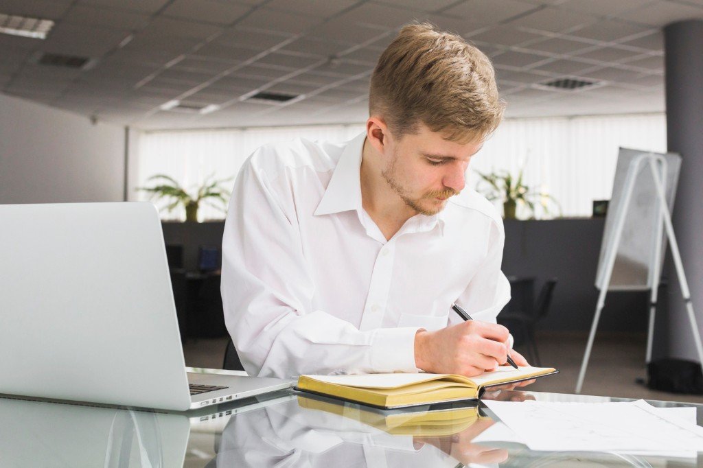 A focused business professional working at a desk with a laptop and notebook in a modern office.